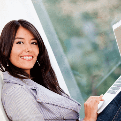 a Native woman sitting on a window ledge holding a laptop